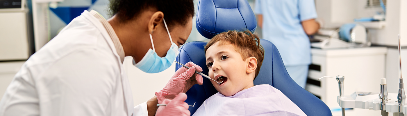 Young child sitting in dentist chair while dentist looks at their teeth