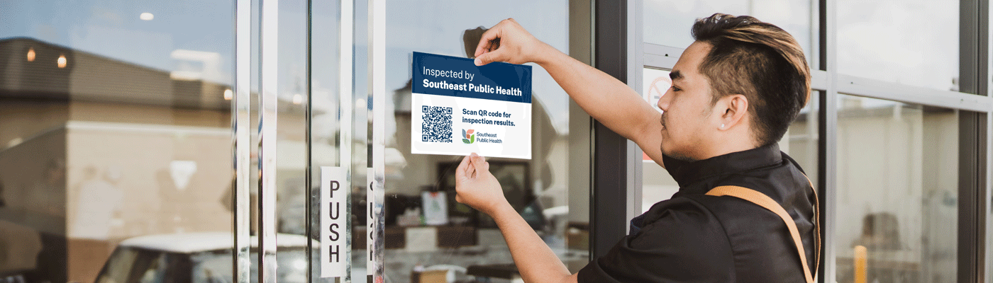 A public health inspector applying an inspected sticker to an establishment's door window