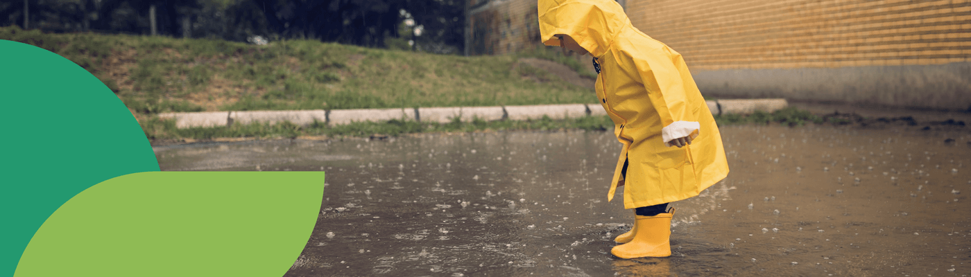 Child wearing a yellow rain jacket and rubber boots splashing in the rain