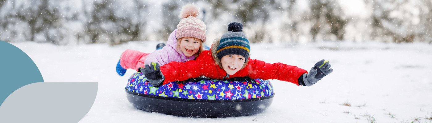 Two children riding on a snow tube downhill in winter