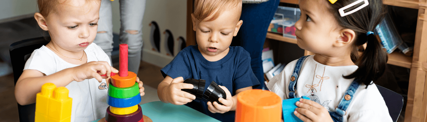Three children playing with rings and blocks at a table
