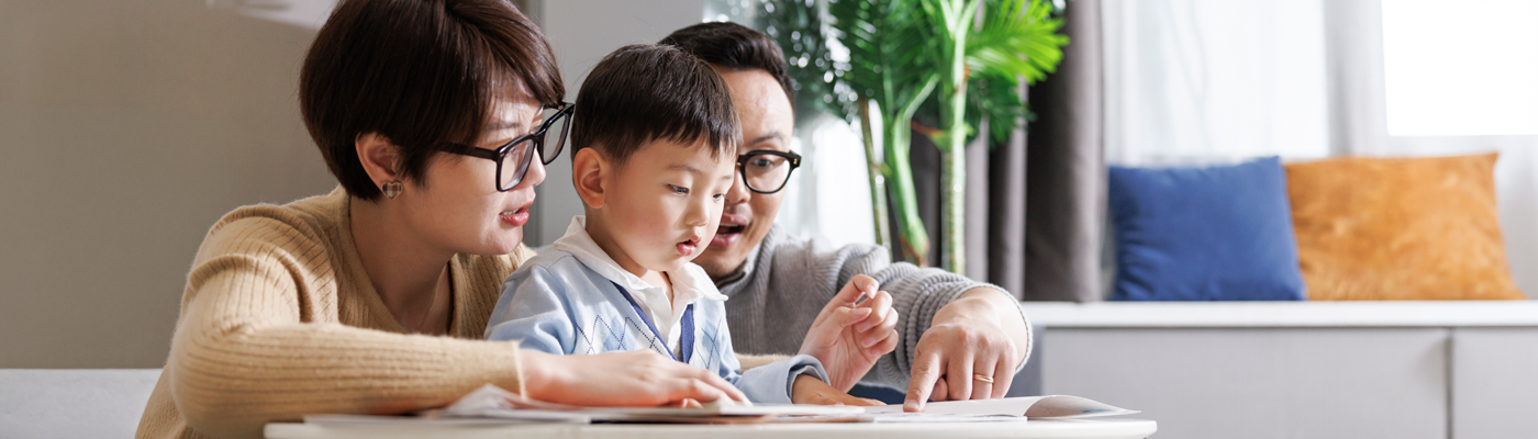 Parents teaching their child how to read a book while pointing at the words