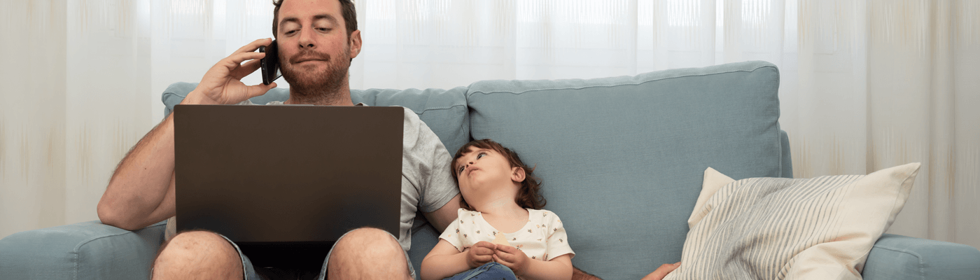 A child and parent sitting on a couch contacting someone on the phone while viewing a laptop